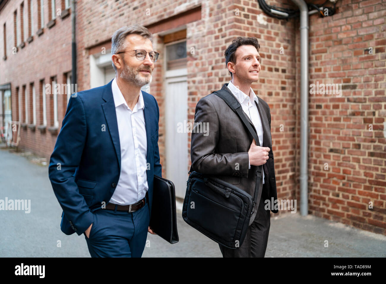 Zwei lächelnde Geschäftsleute gehen mit einem alten Backsteingebäude Stockfoto