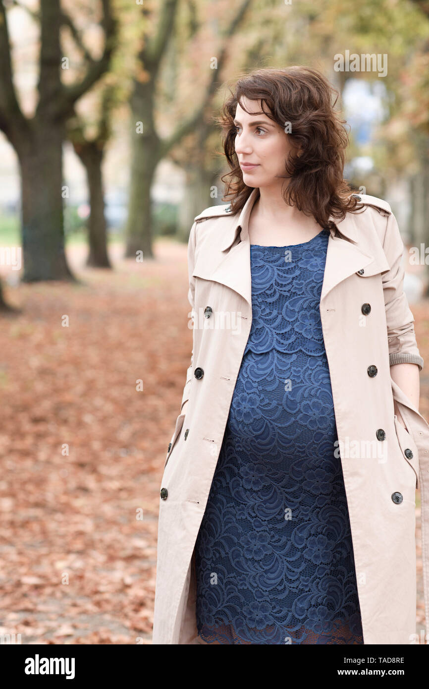 Portrait der schwangeren Frau in Trenchcoat und blauen Kleid im Herbst Stockfoto