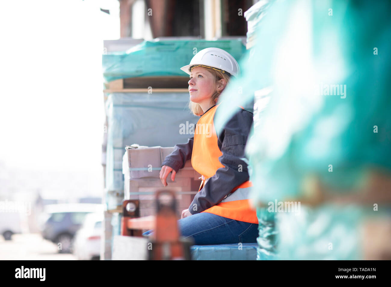 Frau mit Warnweste und Helm sitzen auf Baumaterial Stockfoto