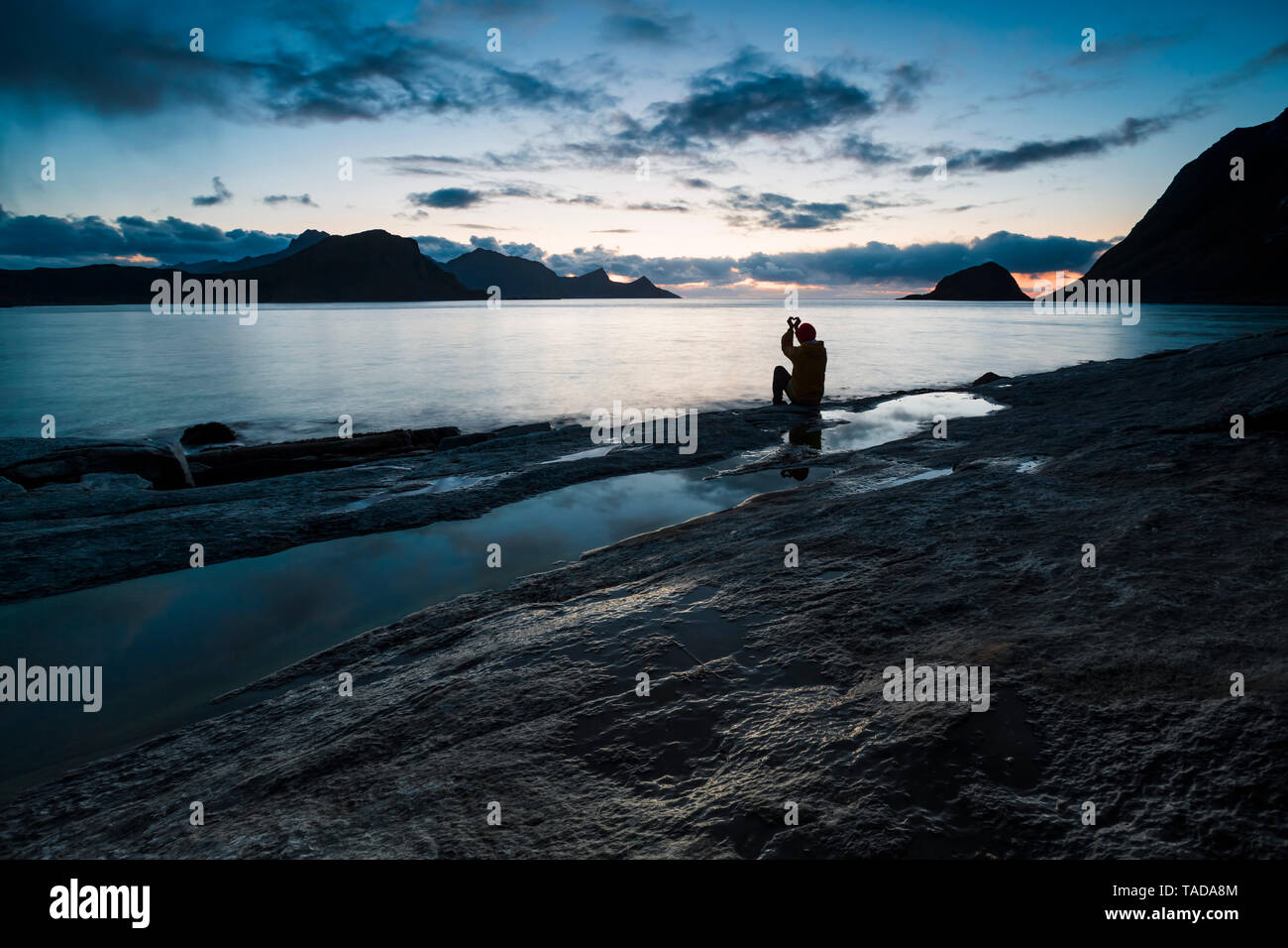 Norwegen, Lofoten, haukland Strand, Mann sitzt auf Felsen, Gebäude Herz mit Finger Stockfoto
