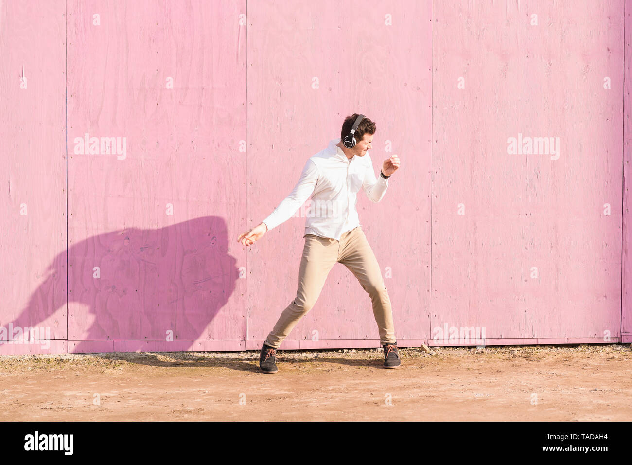 Ausgelassenen jungen Mann hören von Musik vor rosa Wand Stockfoto