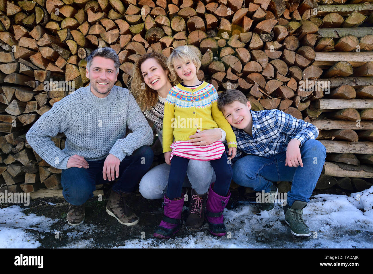 Portrait von Happy Family vor Stapel Holz im Winter Stockfoto