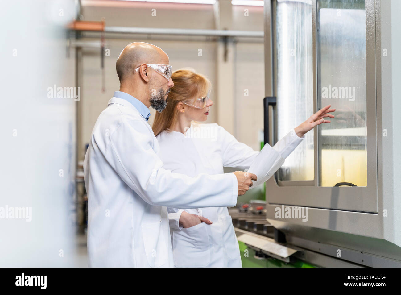 Zwei Techniker tragen Laborkittel und Schutzbrille Maschine prüfen Stockfoto