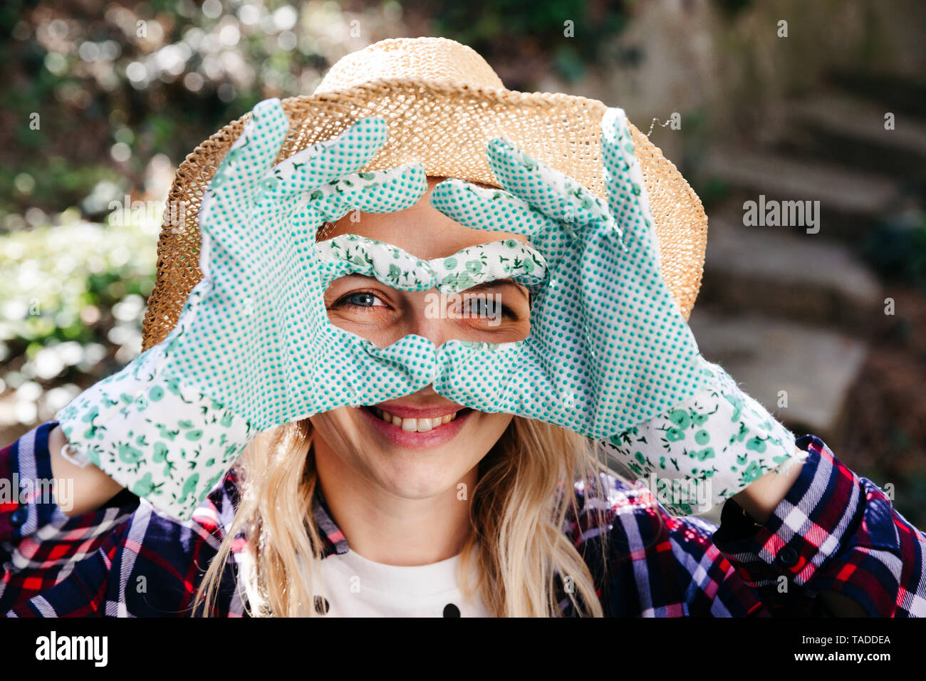 Junge blonde Frau mit Strohhut und grünen Gartenhandschuhe Stockfoto