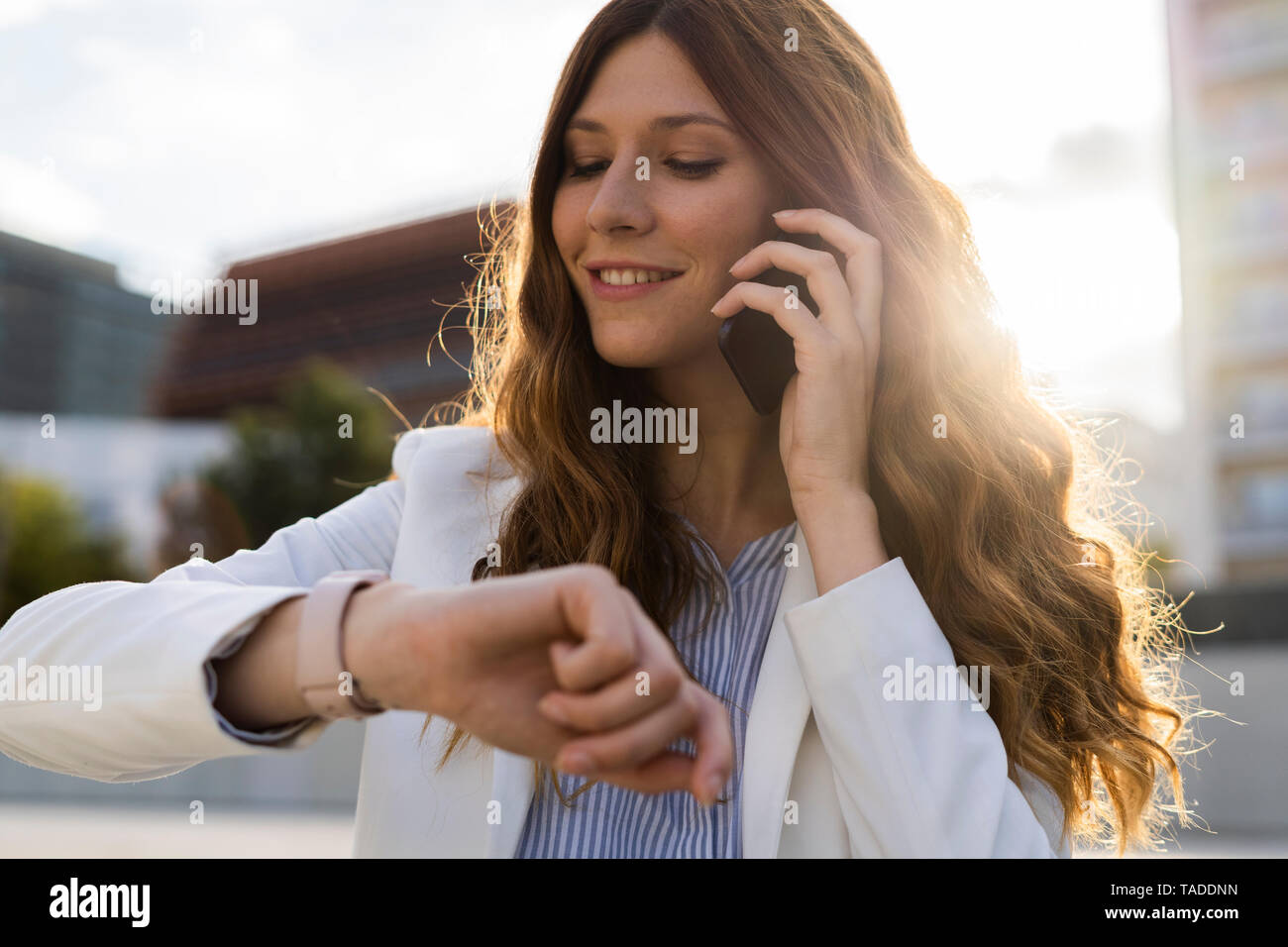 Junge Geschäftsfrau in der Stadt, am Telefon zu sprechen, Kontrolle der Zeit Stockfoto