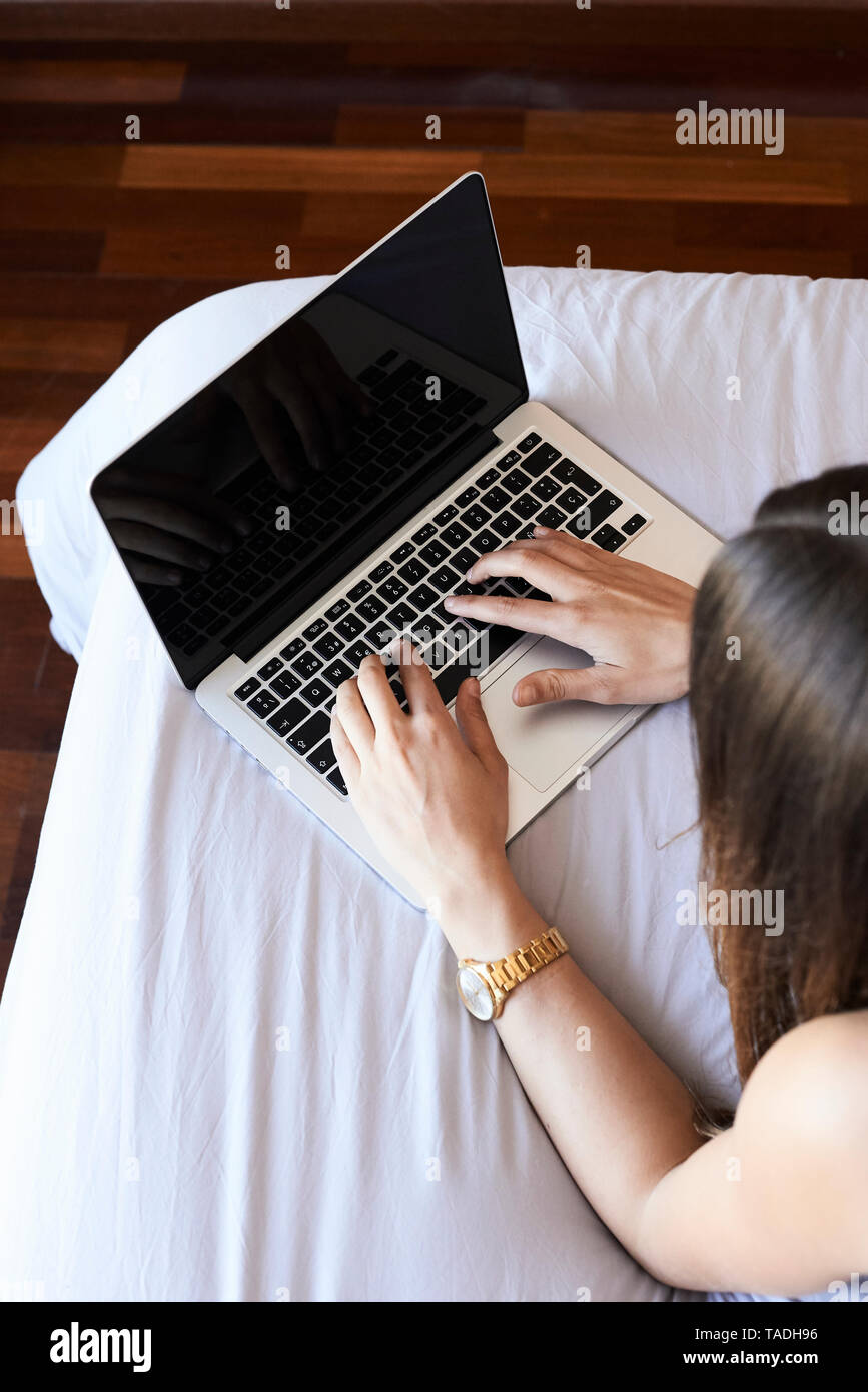 Junge Frau auf dem Bett liegend mit Laptop, Teilansicht Stockfoto