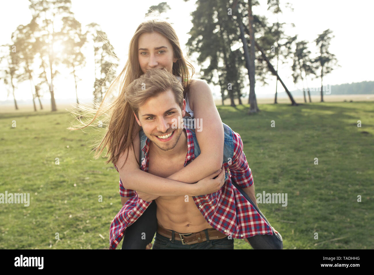 Porträt der glückliche junge Mann, Freundin Huckepack auf Wiese Stockfoto