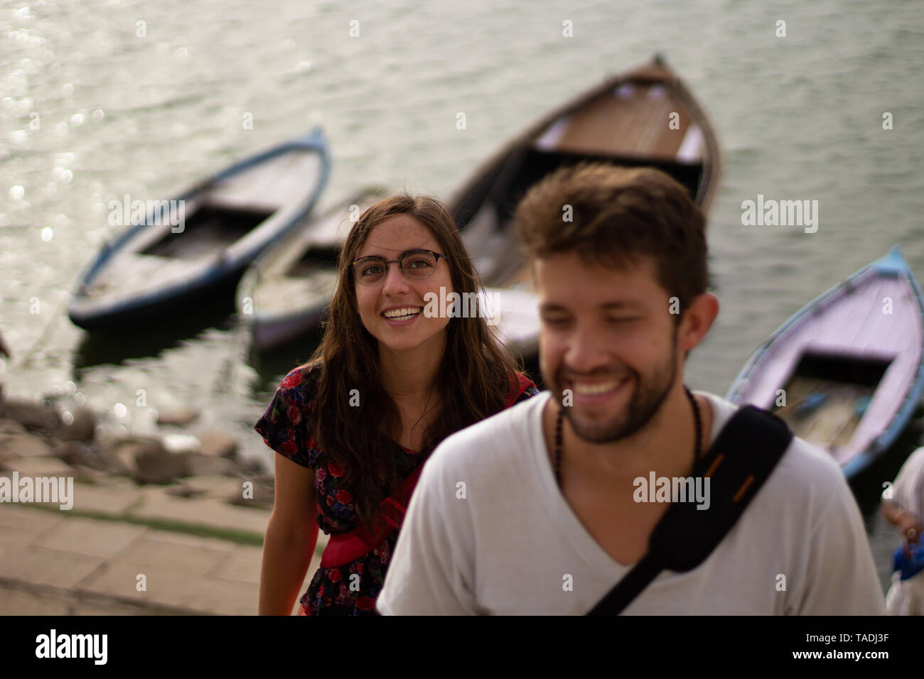 Yong Mann und Frau gehen auf den Stufen des ghats mit varanasi Ganges und hölzerne Boote hinter sich. Stockfoto