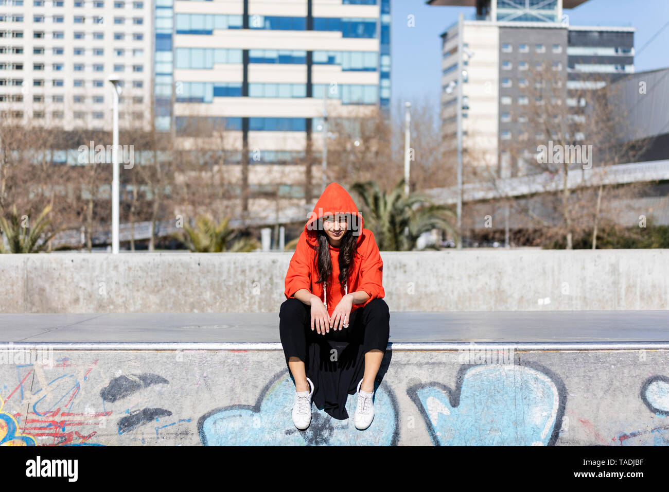 Junge zeitgenössische Tänzerin das Tragen der roten Hoodie T-Shirt, auf dem Boden sitzend mit der Stadt im Hintergrund Stockfoto