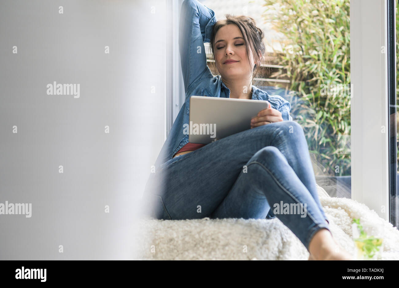 Frau mit Tablet am Fenster zu Hause sitzen mit geschlossenen Augen Stockfoto