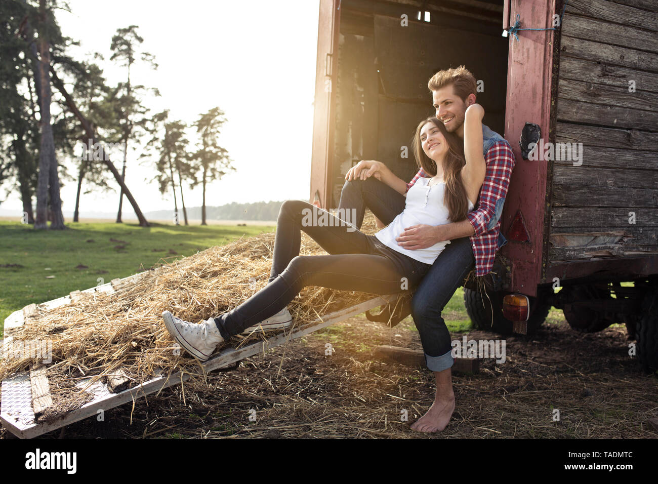 Glückliches junges Paar sitzt auf Trailer in der Landschaft Stockfoto