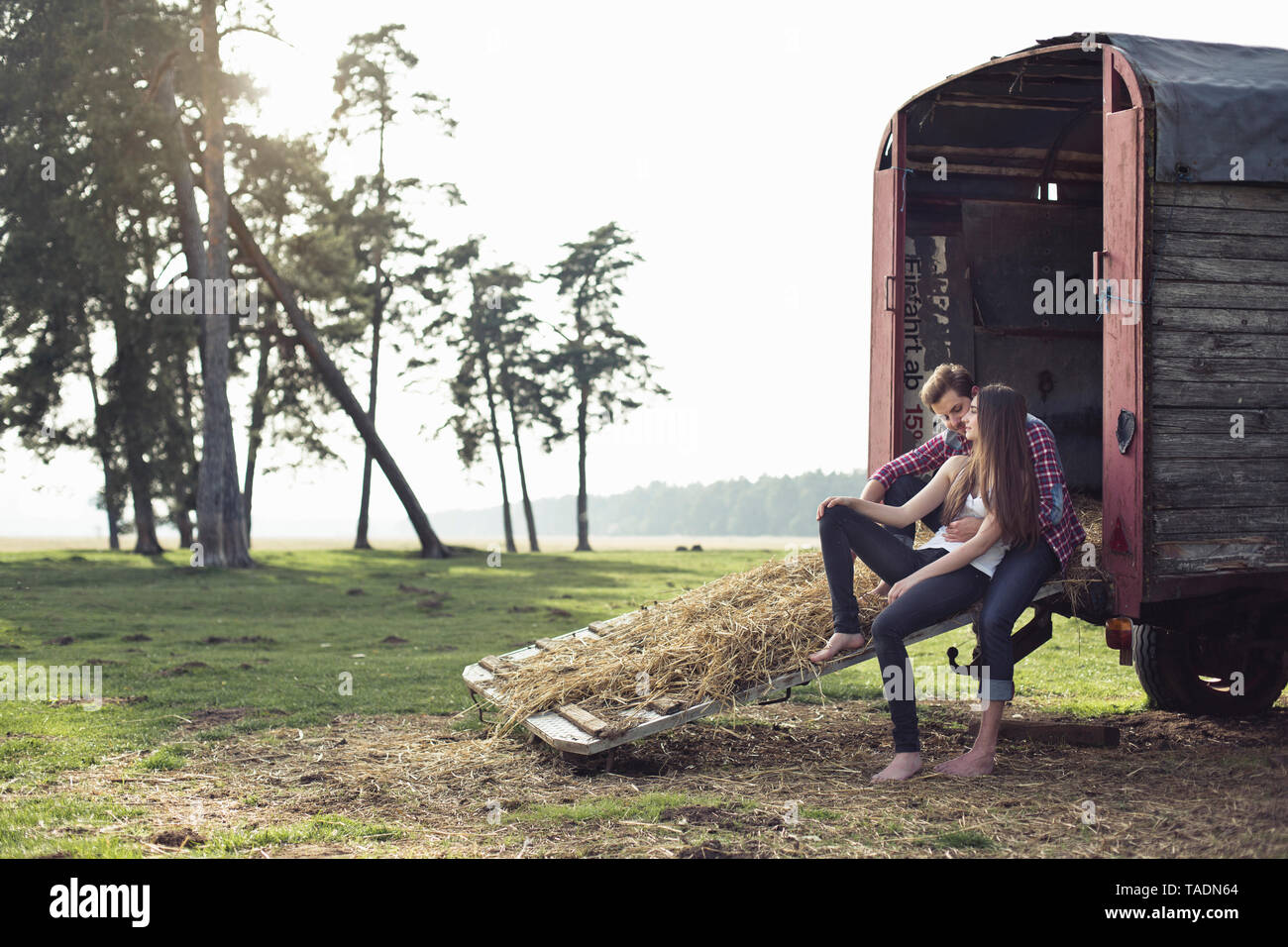 Glückliches junges Paar sitzt auf Trailer in der Landschaft Stockfoto