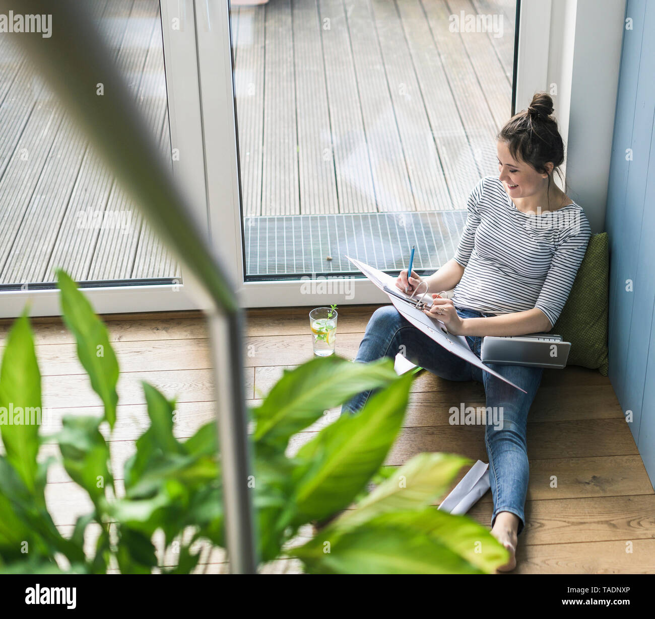 Aus der Vogelperspektive lächelnde Frau am Fenster zu Hause sitzen Arbeiten mit Laptop und Ordner Stockfoto