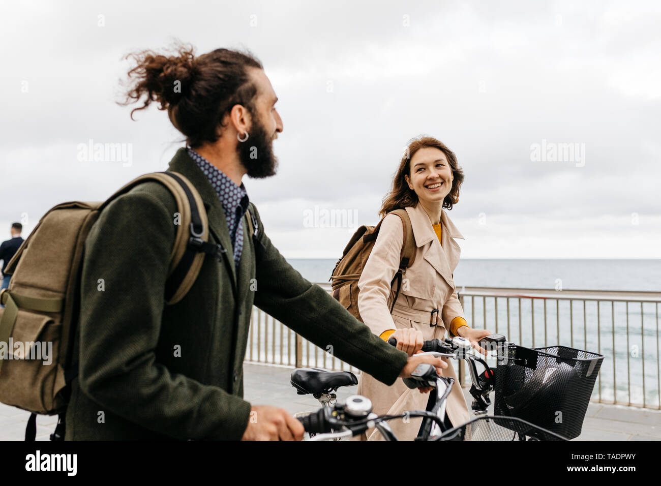 Lächelndes Paar mit e-Bikes auf der Strandpromenade Stockfoto