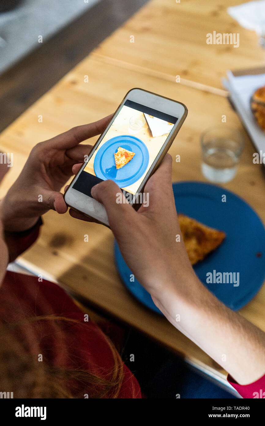 Person, die Smartphone Bild von einem Stück Pizza auf dem Teller Stockfoto