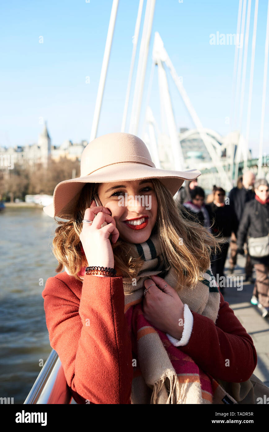 UK, London, stilvolle junge Frau mit Handy über die Millennium Bridge Stockfoto