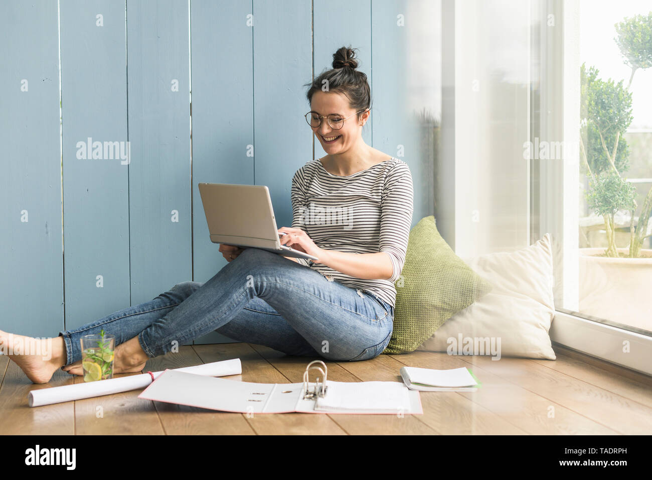 Lächelnde Frau am Fenster zu Hause sitzen Arbeiten mit Laptop und Ordner Stockfoto