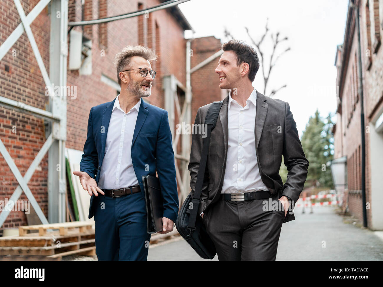 Zwei lächelnde Geschäftsleute zu Fuß und im Gespräch mit einem alten Backsteingebäude Stockfoto