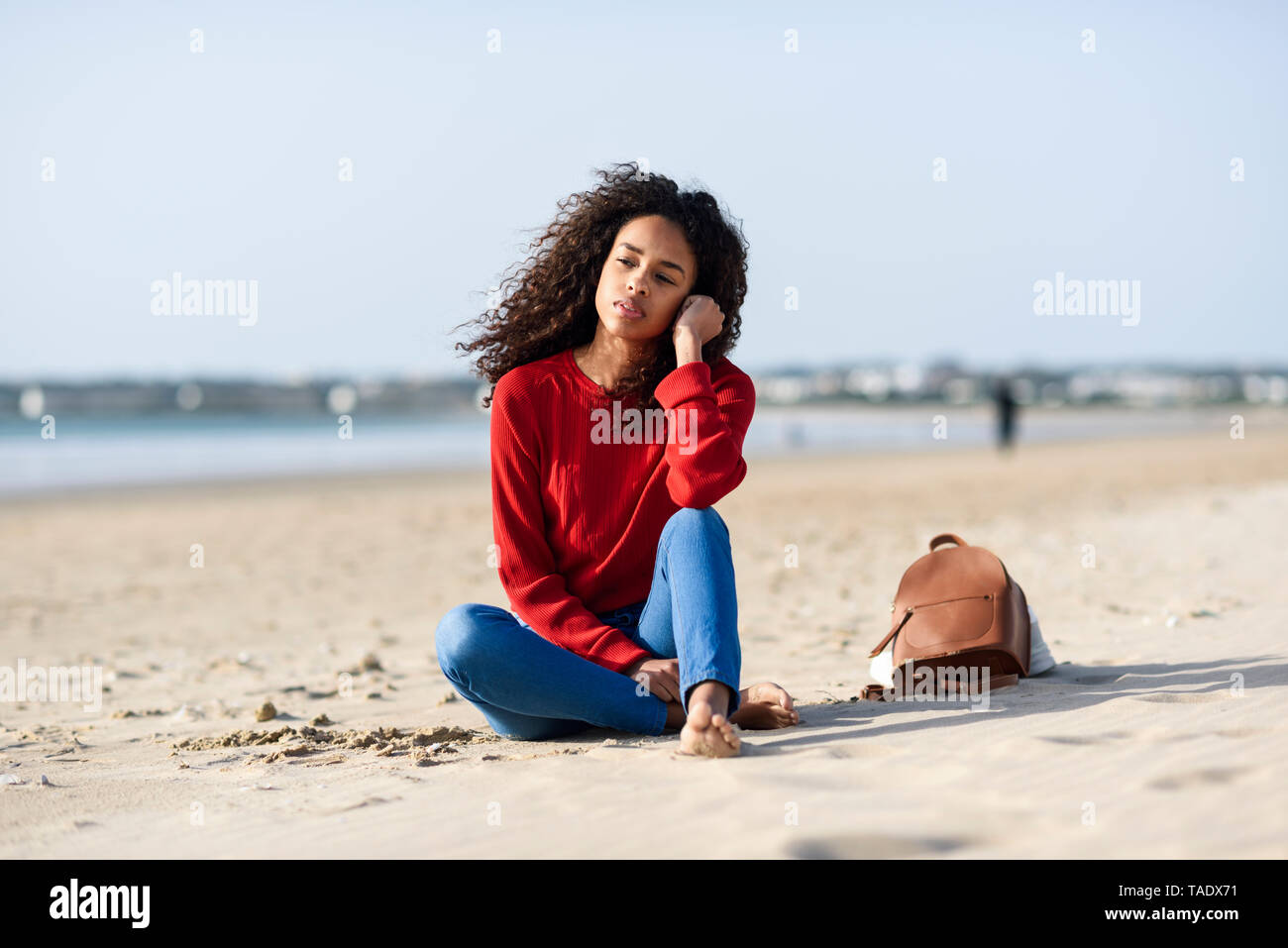 Nachdenkliche junge Frau sitzt am Strand Stockfoto