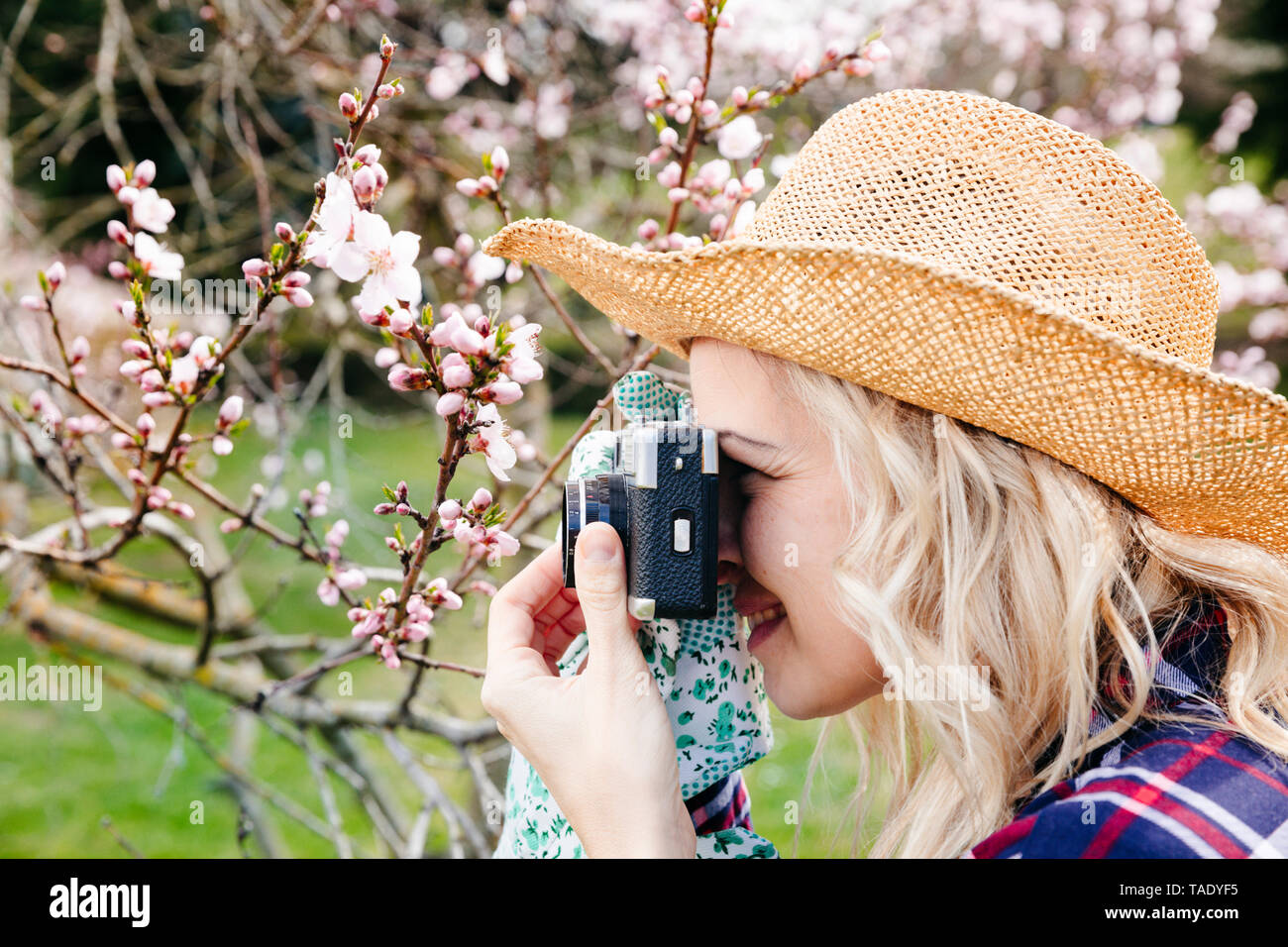 Junge Frau mit einem Strohhut Aufnehmen von Bildern im Garten mit einer alten Kamera Stockfoto