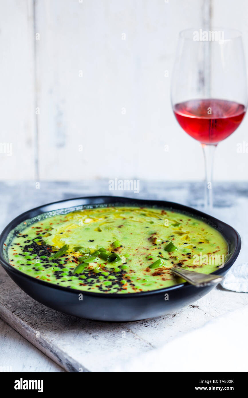 Schale frische grüne Erbsensuppe mit Frühlingszwiebeln und einem Glas Rot Wein Stockfoto