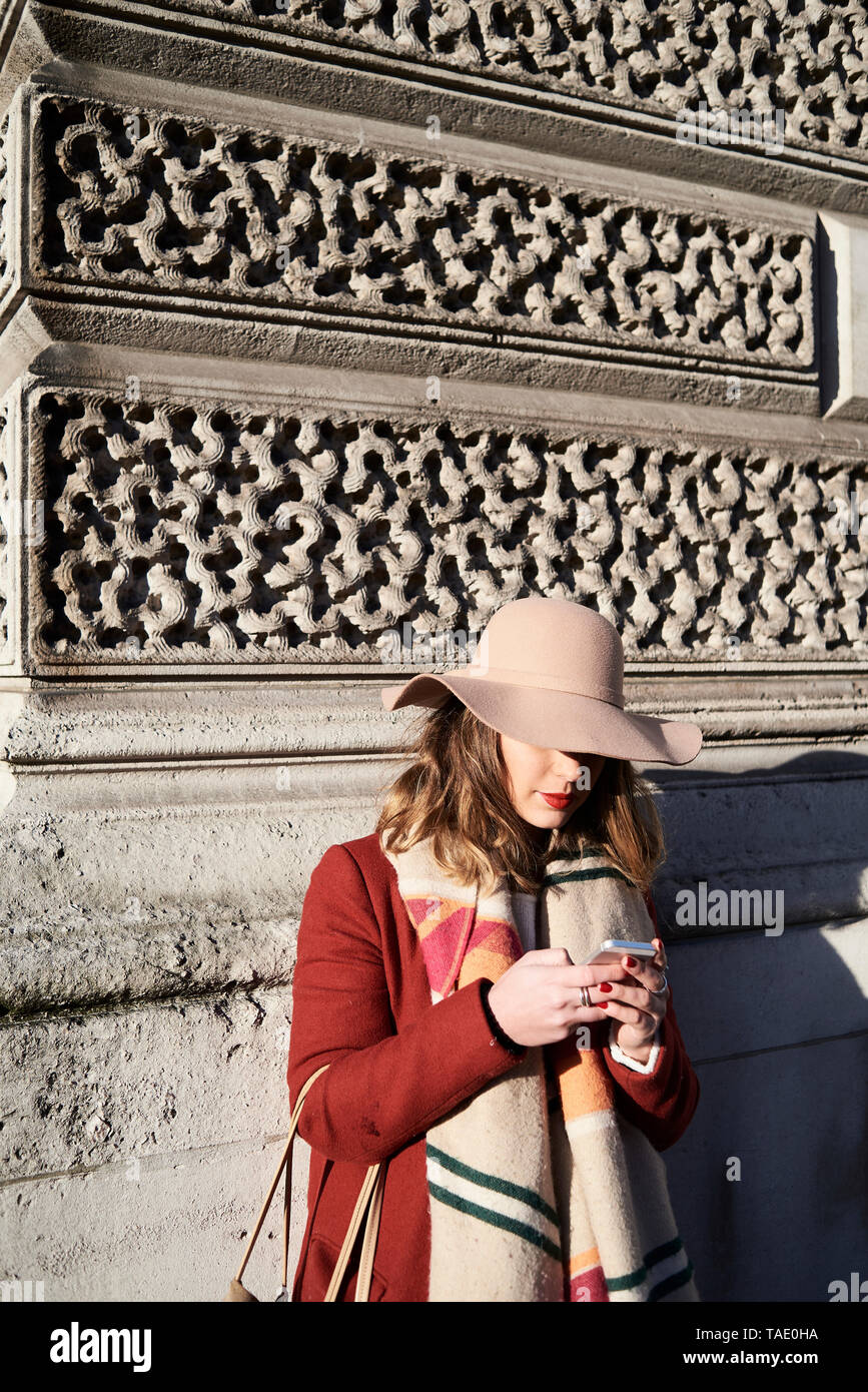 Stilvolle Frau an einem Gebäude tragen eine Diskette hat mittels Handy Stockfoto