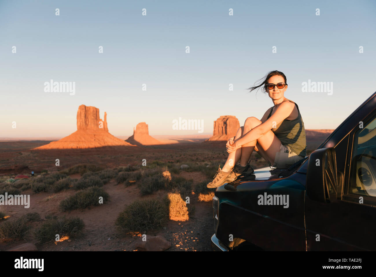 USA, Utah, Monument Valley, Frau sitzt auf der Motorhaube, genießen den Sonnenuntergang im Monument Valley Stockfoto