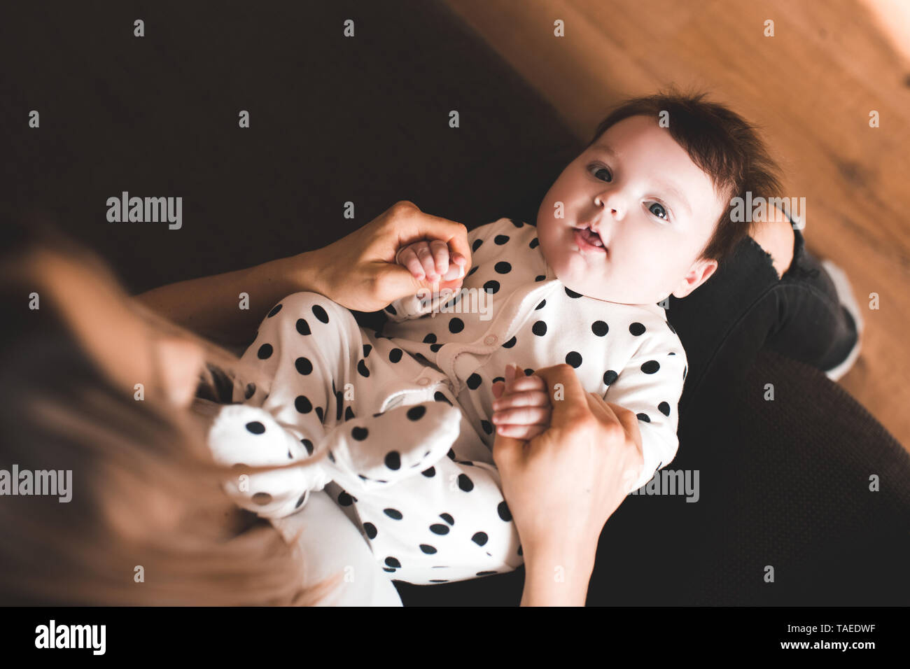 Lustige baby liegend auf Mutter im Zimmer. Mit Blick auf die Kamera. Ansicht von oben. Kindheit. Stockfoto