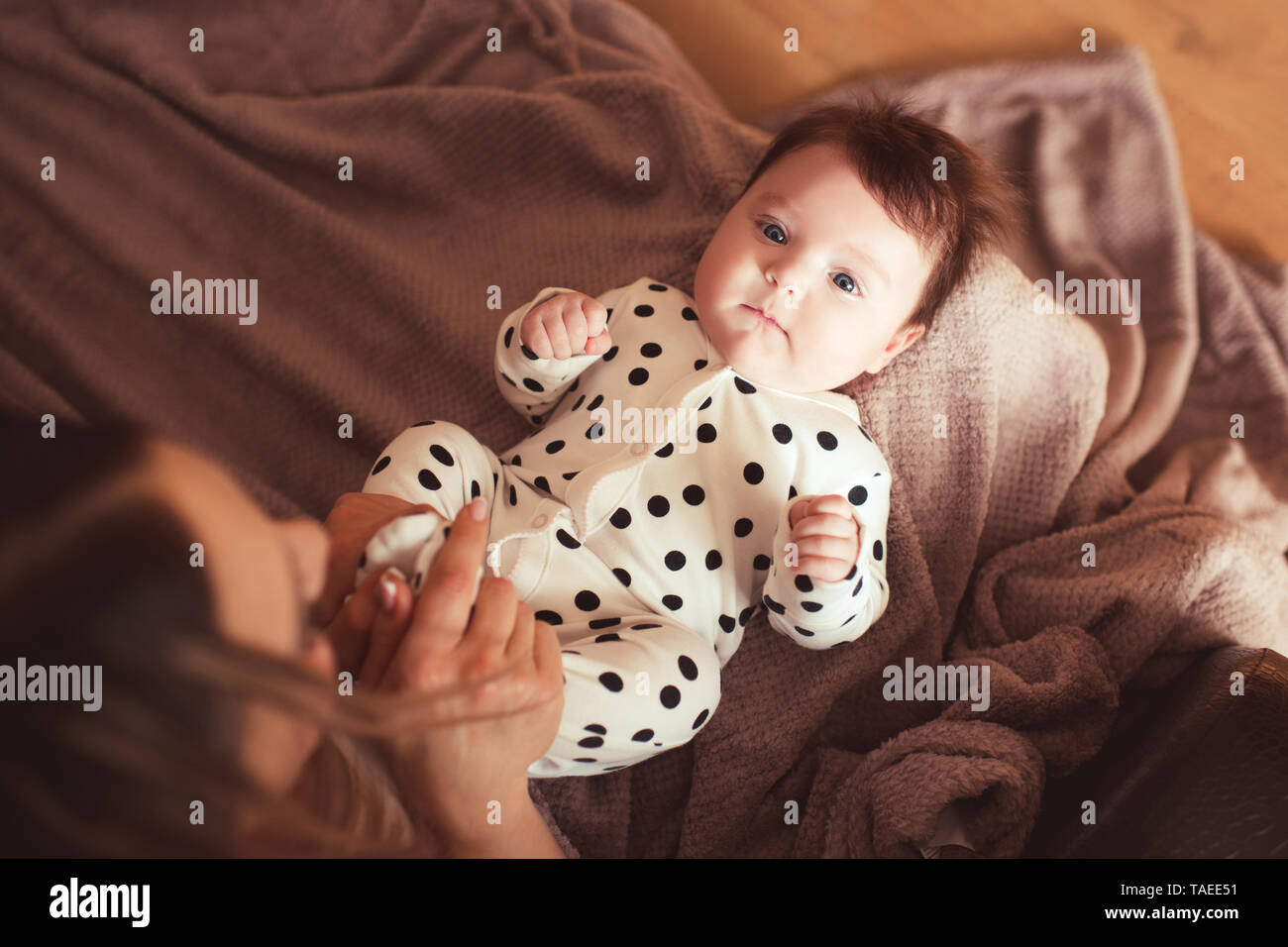 Baby Mädchen liegt in der Mutter Hände auf gestrickte Decke hautnah. Mit Blick auf die Kamera. Die Mutterschaft. Ansicht von oben. Stockfoto