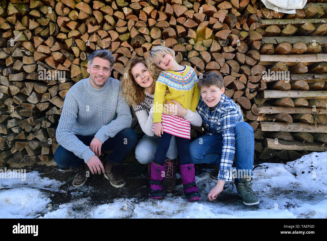 Portrait von Happy Family vor Stapel Holz im Winter Stockfoto