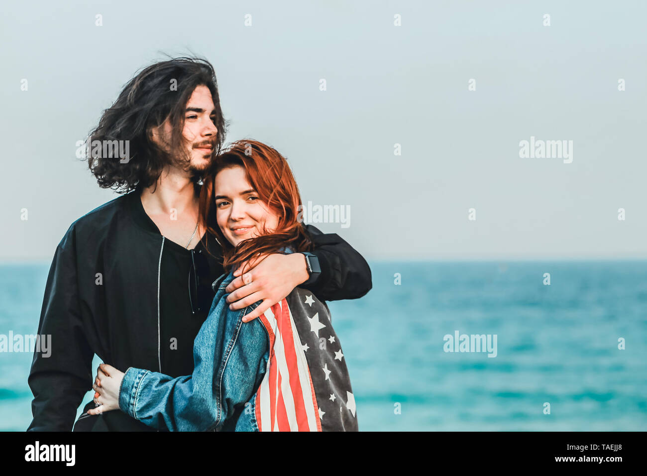 Glückliches junges Paar mit Meerblick auf einem warmen Frühlingstag. Schöner Mann sanft umarmt seine schöne rothaarige Schatz. Stockfoto