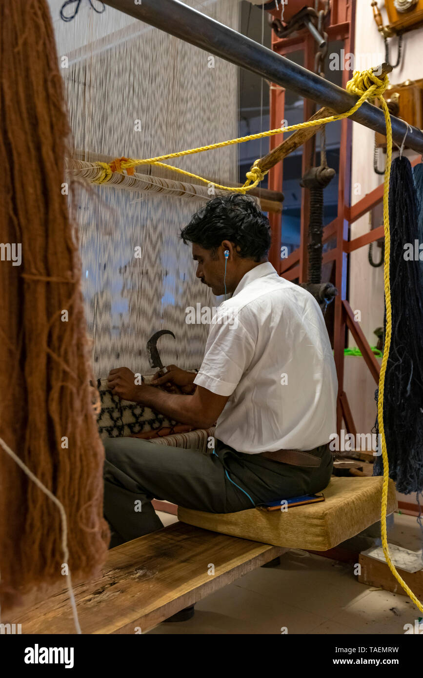 Vertikale Ansicht von einem Mann hören auf sein iphone mit einem altmodischen senkrechten Webstuhl in Indien. Stockfoto