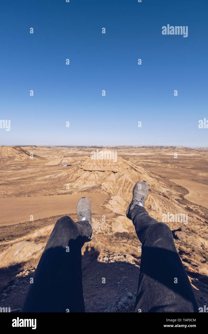 Spanien, Navarra, Bardenas Reales, Beine des Menschen über karge Landschaft baumelt. Stockfoto