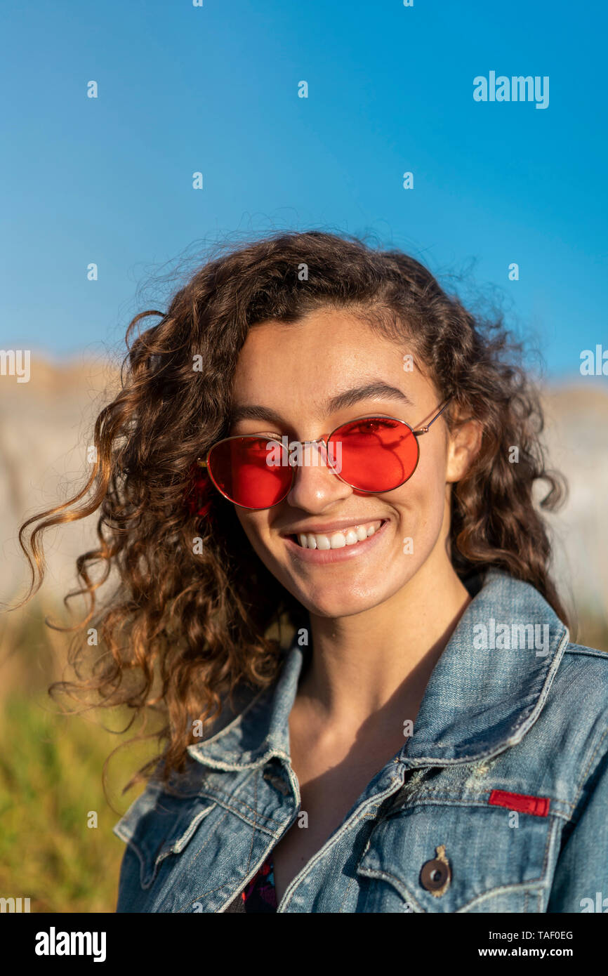 Porträt der glückliche junge Frau mit dem lockigen braunen Haar zu tragen rote Sonnenbrille Stockfoto