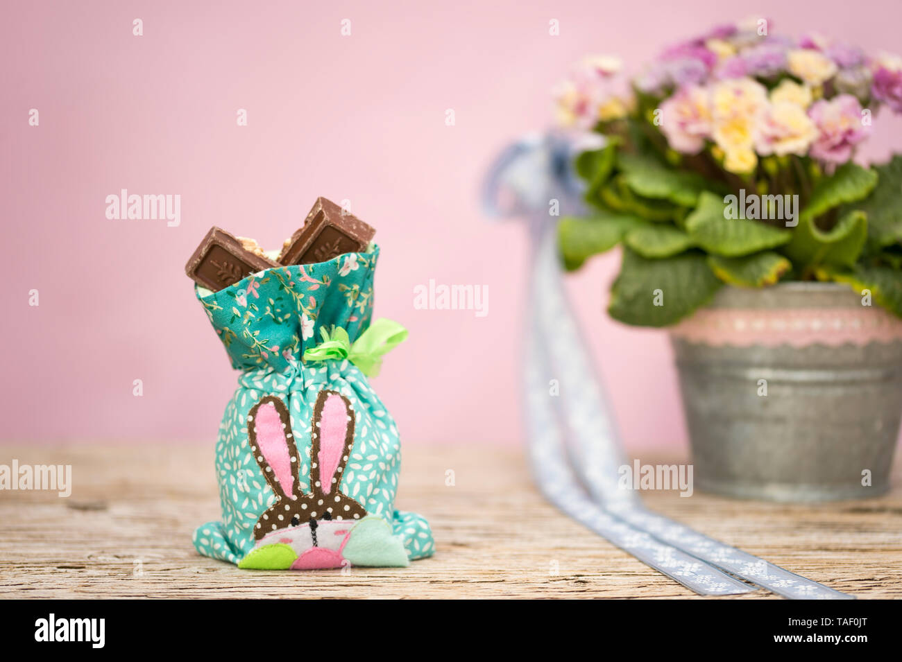 Eine kleine Tasche ist mit Schokolade gefüllt. Ein Osterhase angewandt wurde. Dieses Flickwerk ist vor Frühling Blumen Primeln in Zink Blumentopf. Rosa zurück Stockfoto