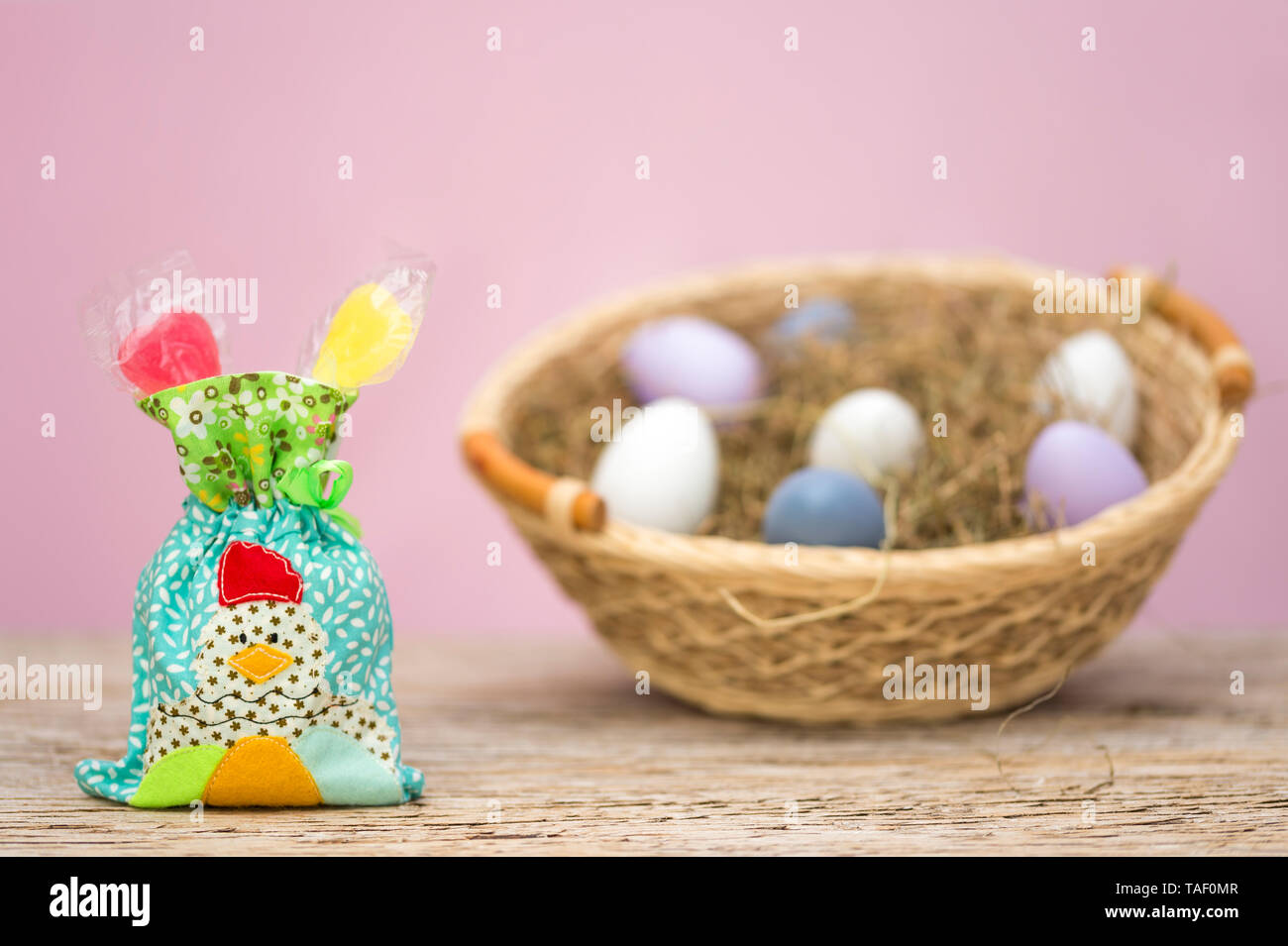 Eine kleine Tüte mit Süßigkeiten gefüllt. Ein Huhn angewandt wurde. Dieses patchwork steht vor einem Nest mit Ostereiern. Rosa Hintergrund mit kopieren. Stockfoto
