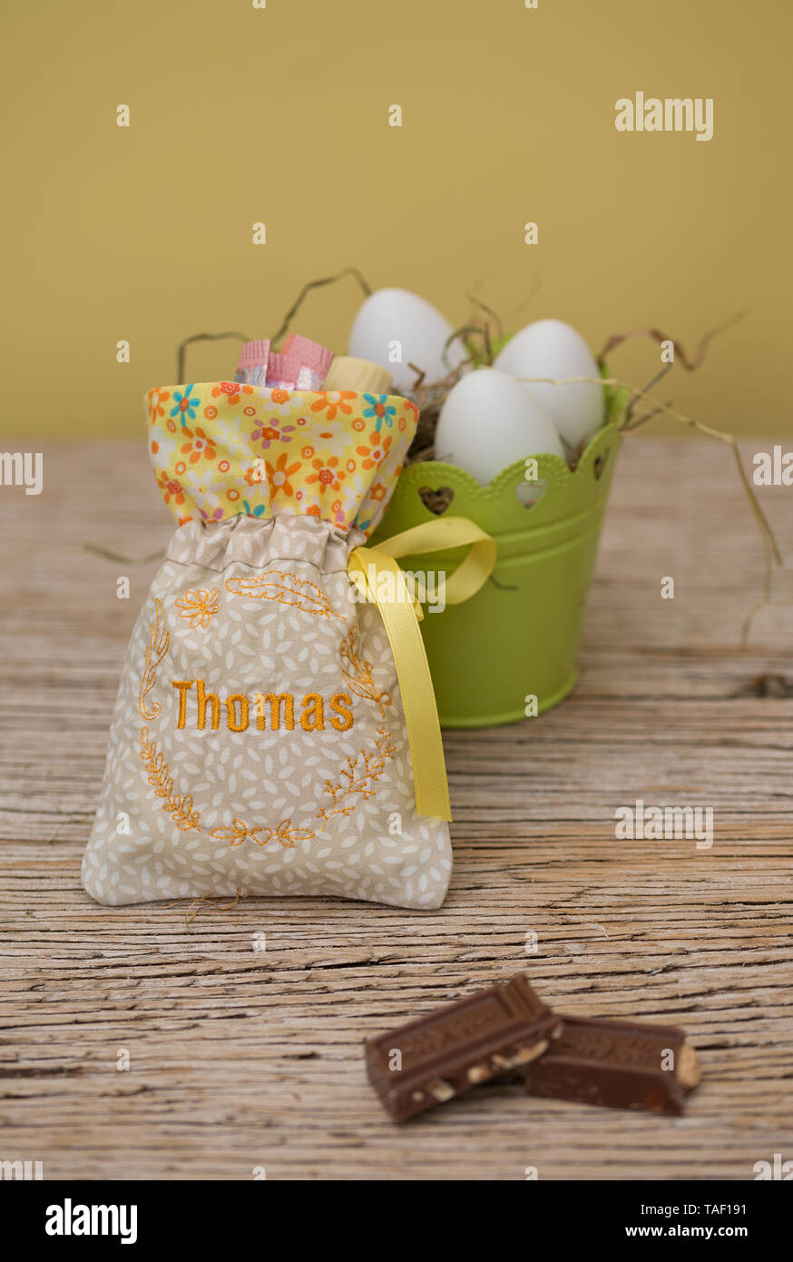 Eine kleine Tasche mit Geschenken hat einen hübschen Stickerei. Es ist der Name Thomas. Hinter der Tasche ist Platz und ein Easter Nest mit Eiern zu kopieren. Pastellfarbenen natur Stockfoto