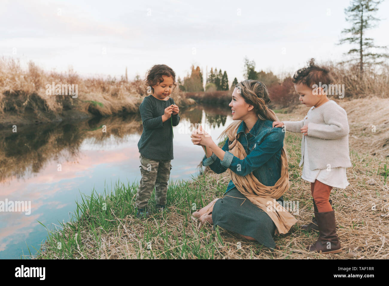 Maother und Kinder spielen mit einem Gras Blade an einem Fluss Stockfoto