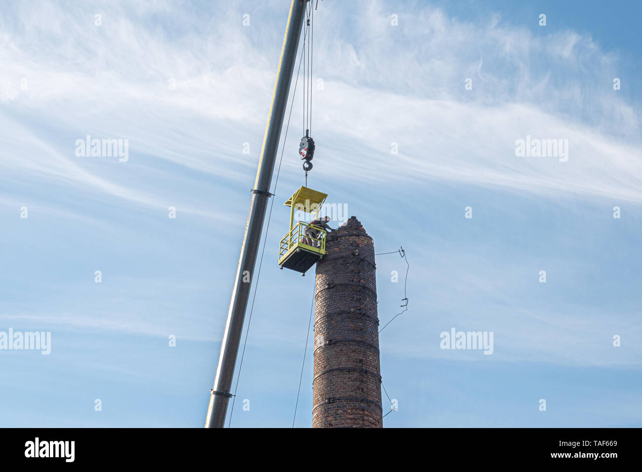 2 Männer in einem Korb hängen von einem riesigen Kran, sorgfältig entfernen einer Fabrik Schornstein Stockfoto