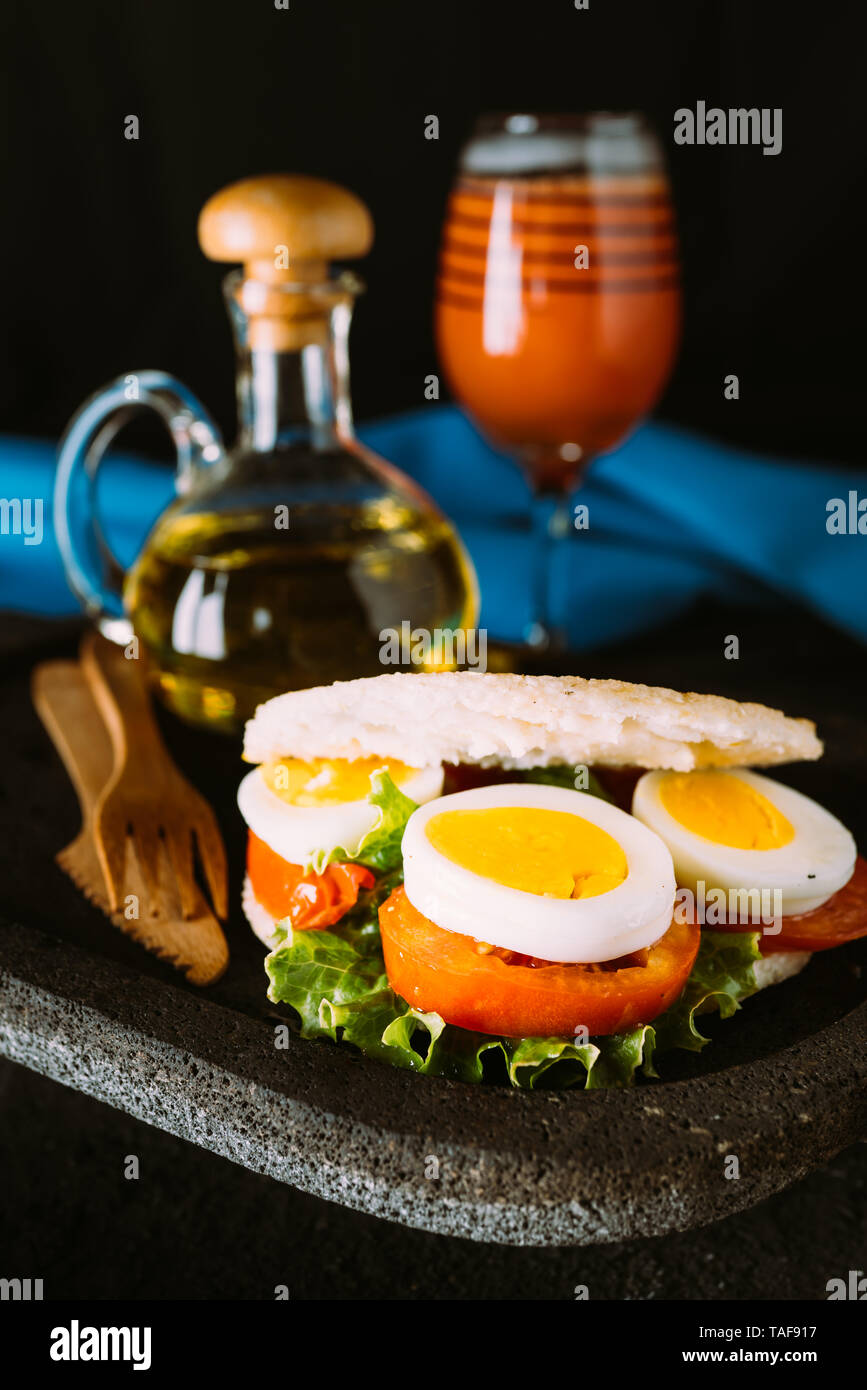Arepa mit Ei und Gemüse zum Frühstück, serviert auf einem vulkanischen Stein Platte mit einem Glas Papayasaft Stockfoto