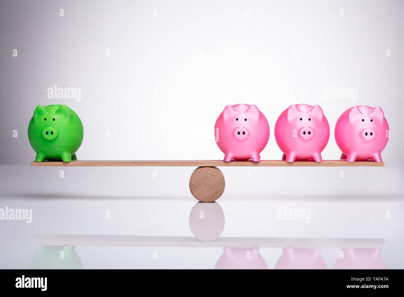 Grün und rosa Sparschwein Balancieren auf Holz- Wippe über reflektierende Schreibtisch Stockfoto