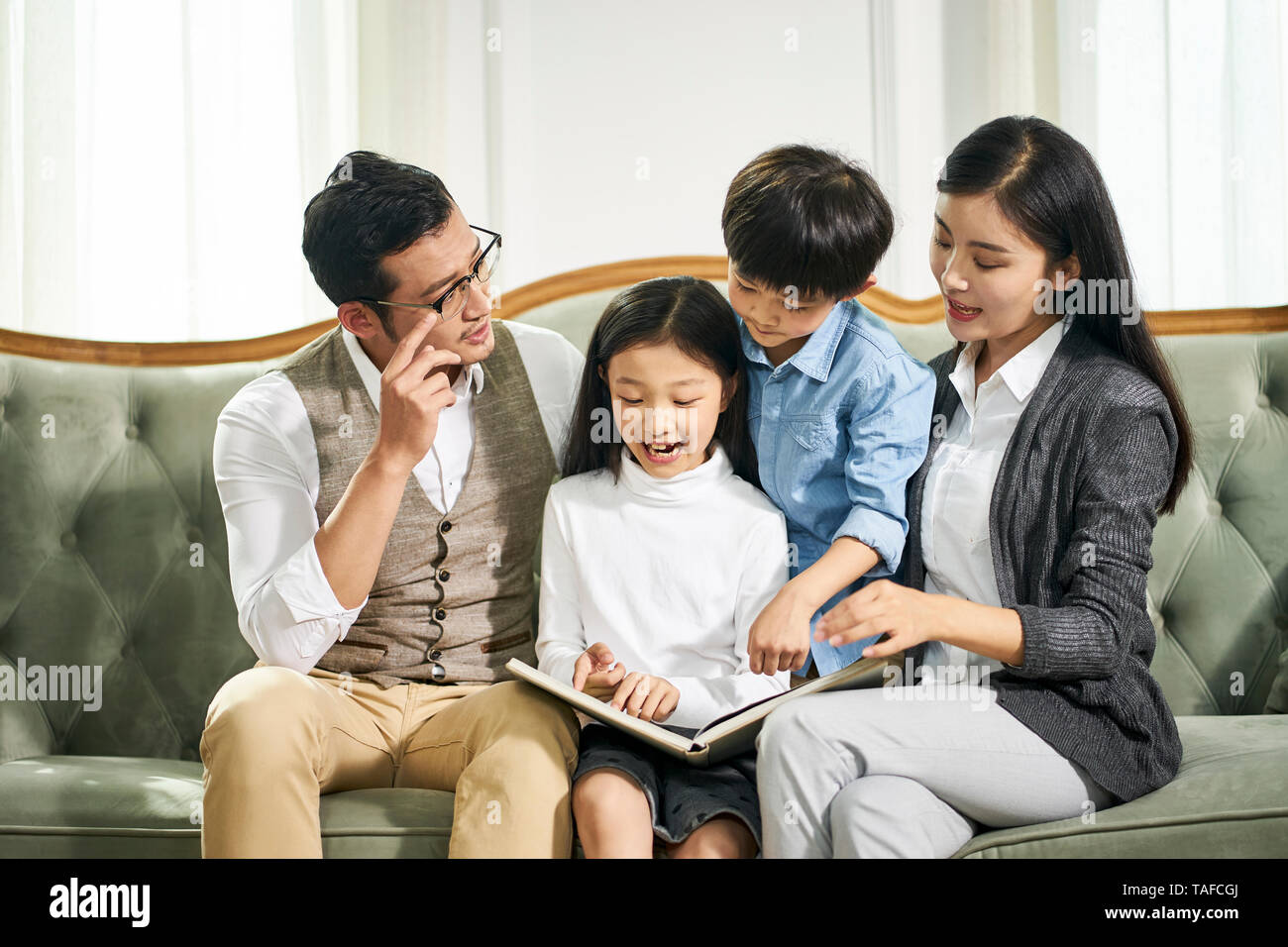 Jungen asiatischen Vater und Mutter und zwei Kindern zusammen auf der Couch lesen Buch Familie sitzen im Wohnzimmer zu Hause Stockfoto