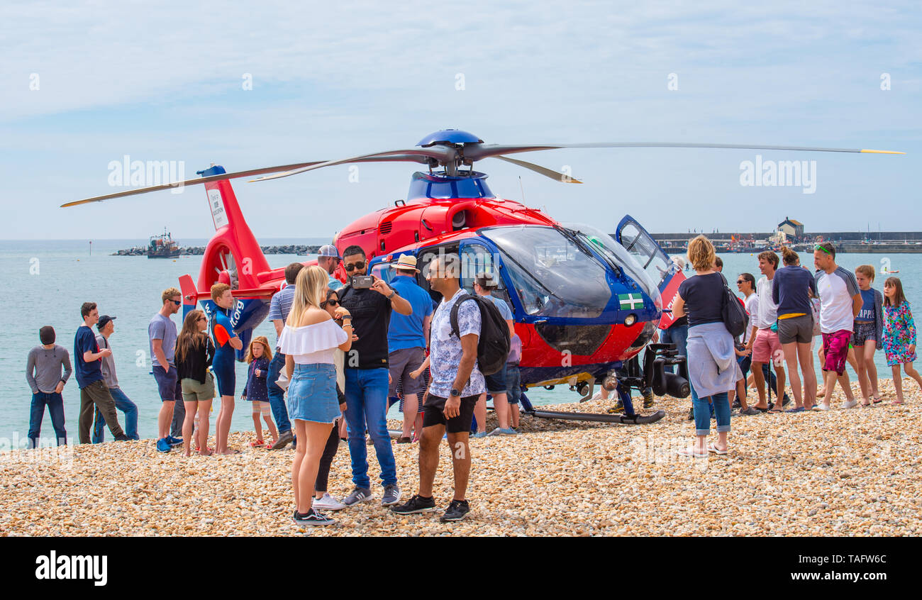 Lyme Regis, Dorset, Großbritannien. 25. Mai 2019. UK Wetter: Massen von Touristen und Besucher in Scharen zu den Strand in Lyme Regis in der heißen Sonne aalen. Die Devon Air Ambulance helicopter erzeugt das Interesse der Zuschauer, wie es zu einem Notfall auf dem belebten Strand besucht. Credit: Celia McMahon/Alamy Leben Nachrichten. Credit: Celia McMahon/Alamy leben Nachrichten Stockfoto