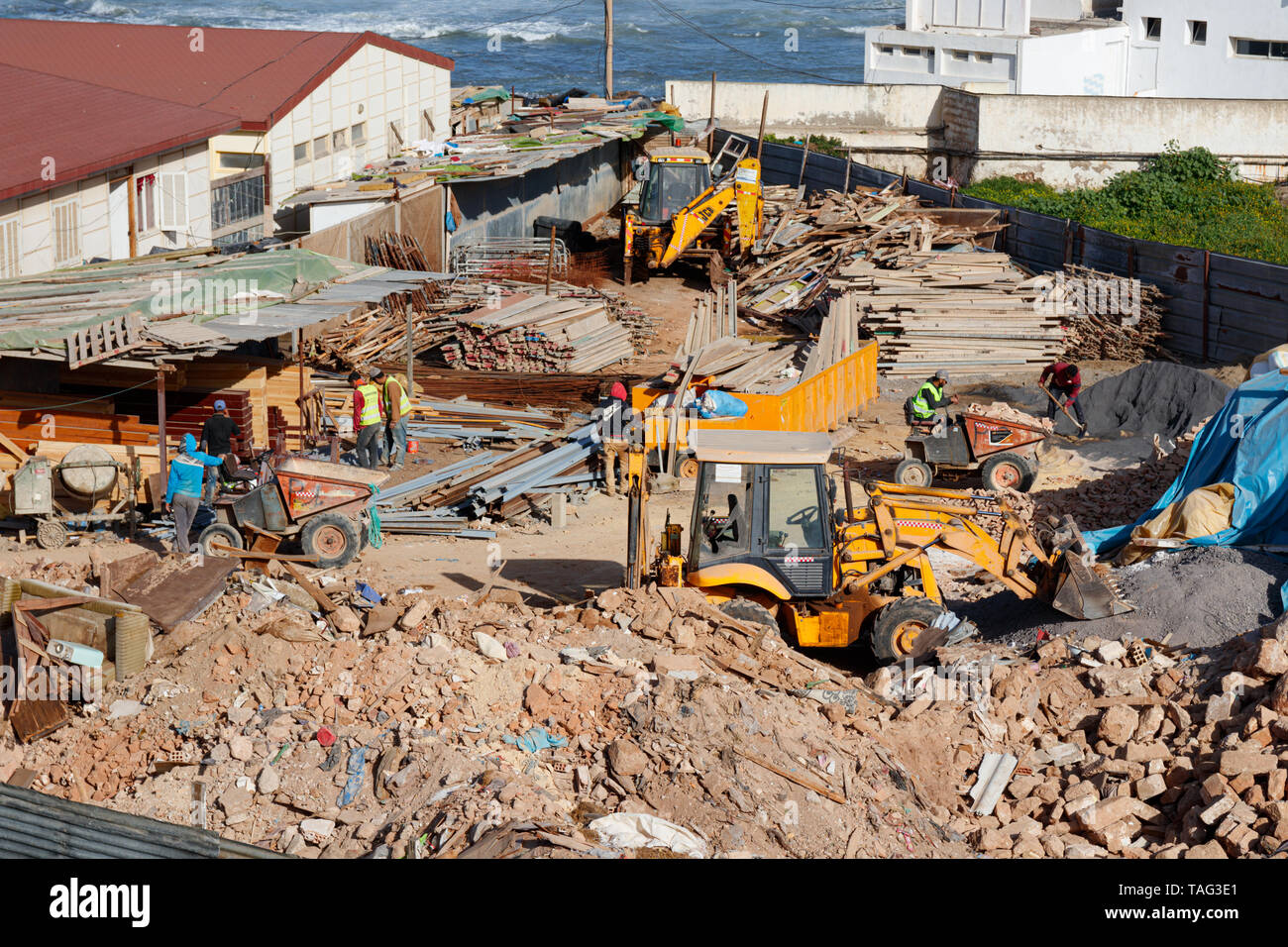 Construction Yard an der Küste von Rabat mit Arbeiter mit Baggerlader und Dumper zu diplace Schutt. Rabat, Marokko. Stockfoto