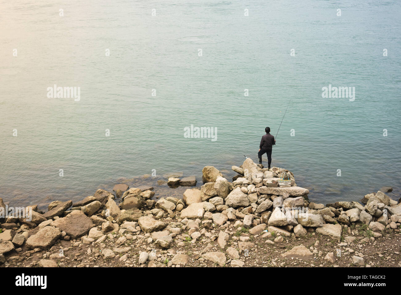 Einsame asiatische Fischer stehen auf Felsen vor der schönen Wasser Stockfoto
