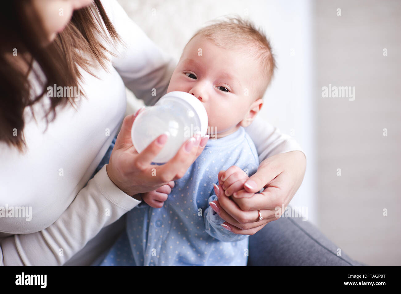 Mutter feeding baby boy liegen auf Hände im Zimmer. Mit Blick auf die Kamera. Motehrhood. Gesunde Ernährung. Stockfoto