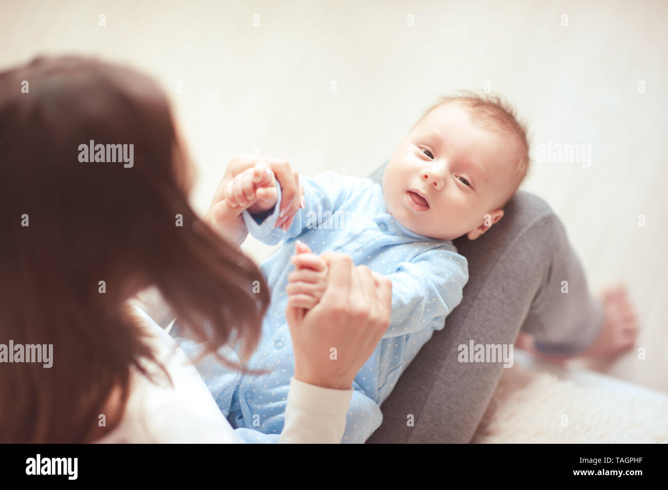 Cute Baby Boy liegen auf Mutter Beine in Nahaufnahme. Frau mit Kind die Hände. Die Mutterschaft. Mutterschaft. Stockfoto