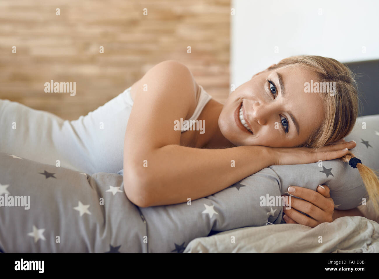Glückliche gesunde junge schwangere Frau ruht auf einem Bett mit einem speziellen Kissen als Unterstützung in die Kamera schaut mit einem reizenden Lächeln Stockfoto