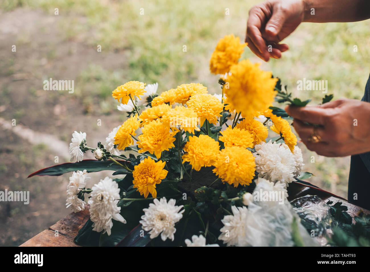 Florist Hände einen Blumenstrauß aus gelben und weißen Chrysantheme auf einem Holztisch. Selektive konzentrieren. Kopieren Sie Platz. Stockfoto