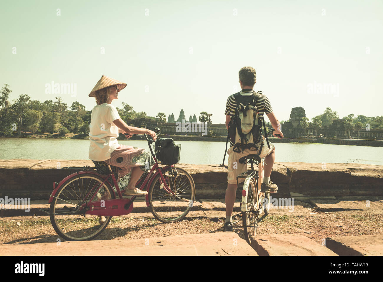 Touristische paar Radfahren im Tempel Angkor, Kambodscha. Angkor Wat Hauptfassade auf Wasser Teich wider. Umweltfreundliche Tourismus reisen. Getönten vintage Stockfoto